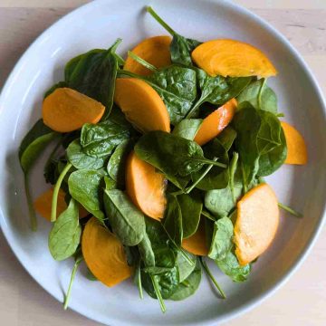 add spinach green and sliced sharon fruit to plate